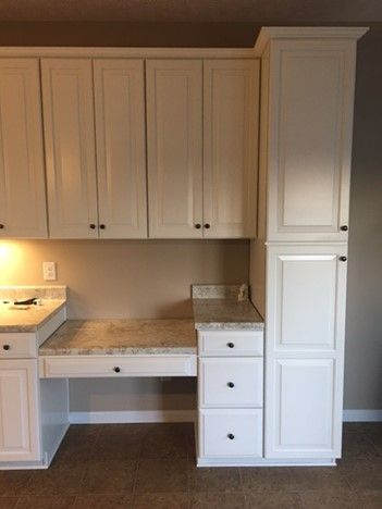 A kitchen with white cabinets and a desk in the corner.