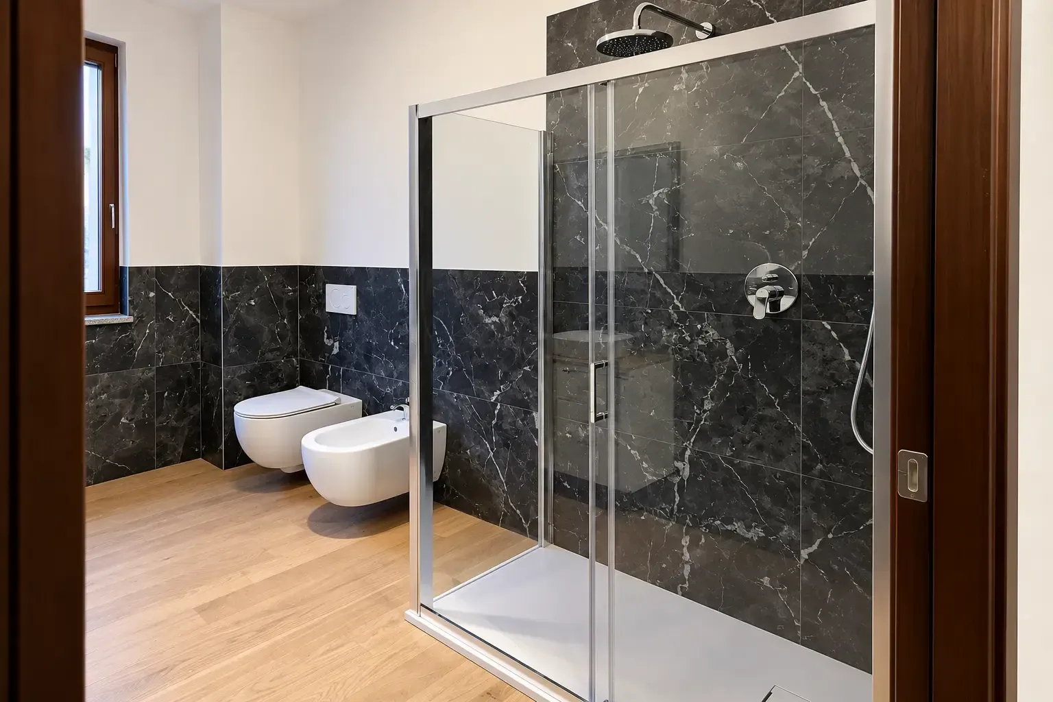 Bagno moderno con pareti in marmo nero, pavimento in legno, bidet e WC bianchi e box doccia in vetro