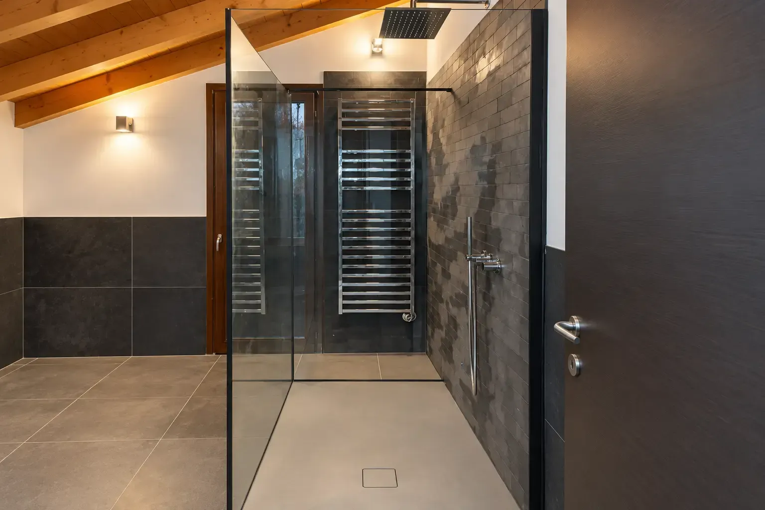 Doccia moderna in un bagno con porta in vetro, pareti piastrellate e soffitto con travi in legno