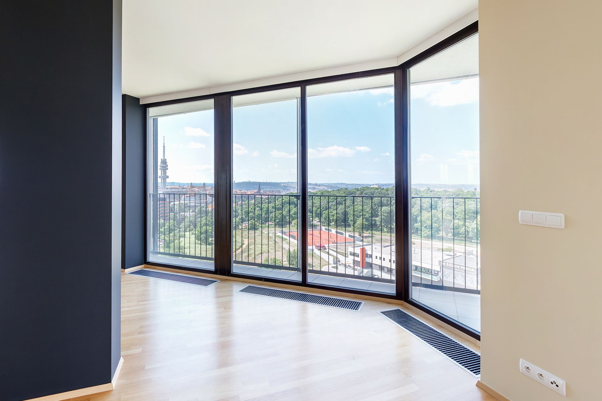 Ampia stanza luminosa con finestre a tutta altezza e vista sulla città, pareti nere e pavimento in legno chiaro