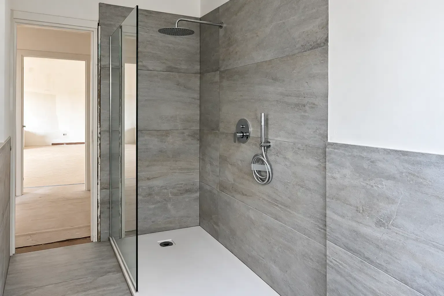 Moderna doccia walk-in piastrellata con pannello in vetro, rubinetteria cromata e piatto doccia bianco