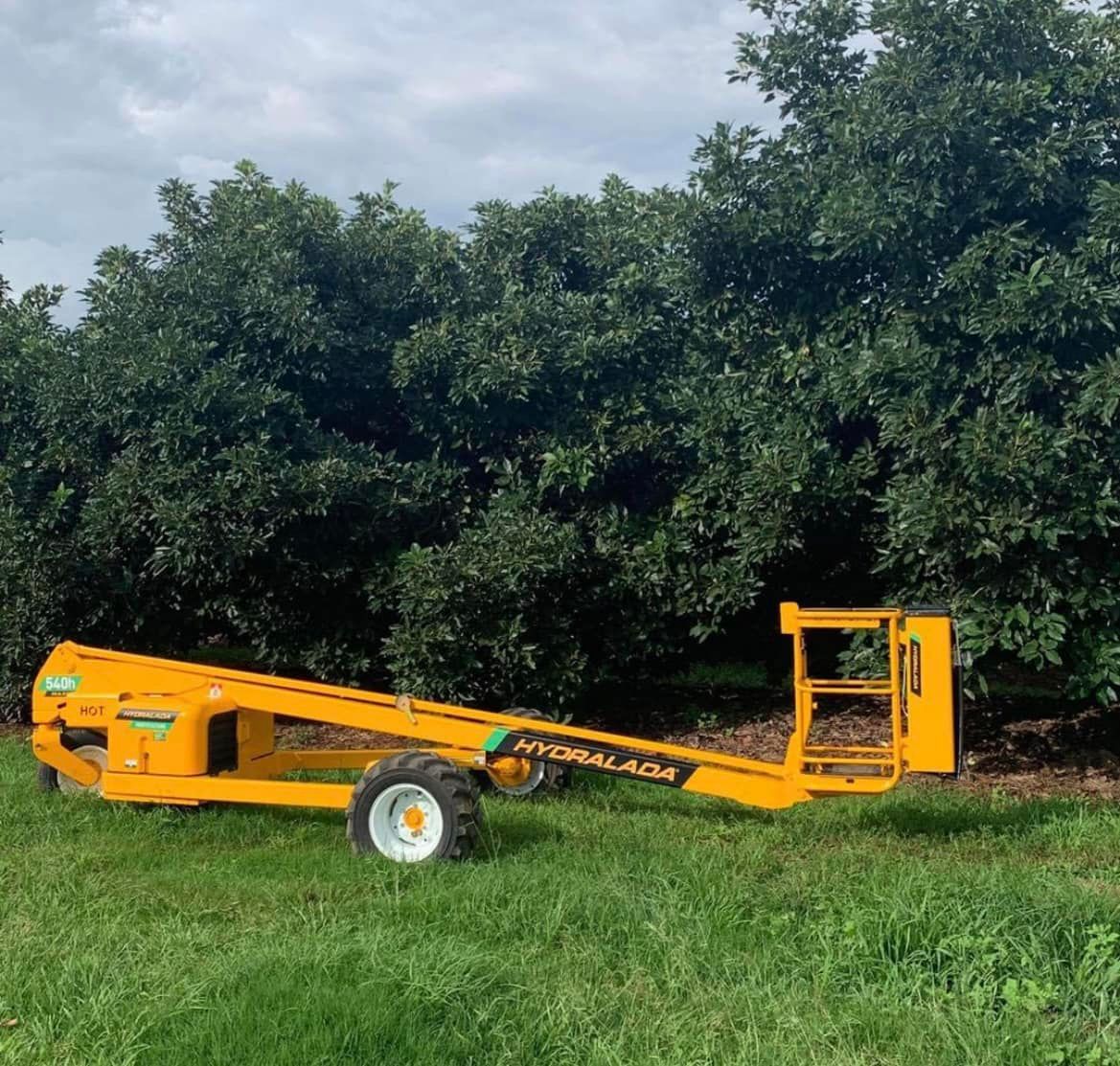 Yellow Towable Boom Lift Parked on Grass in Front of Dense Green Trees — Casali's in Mareeba, QLD