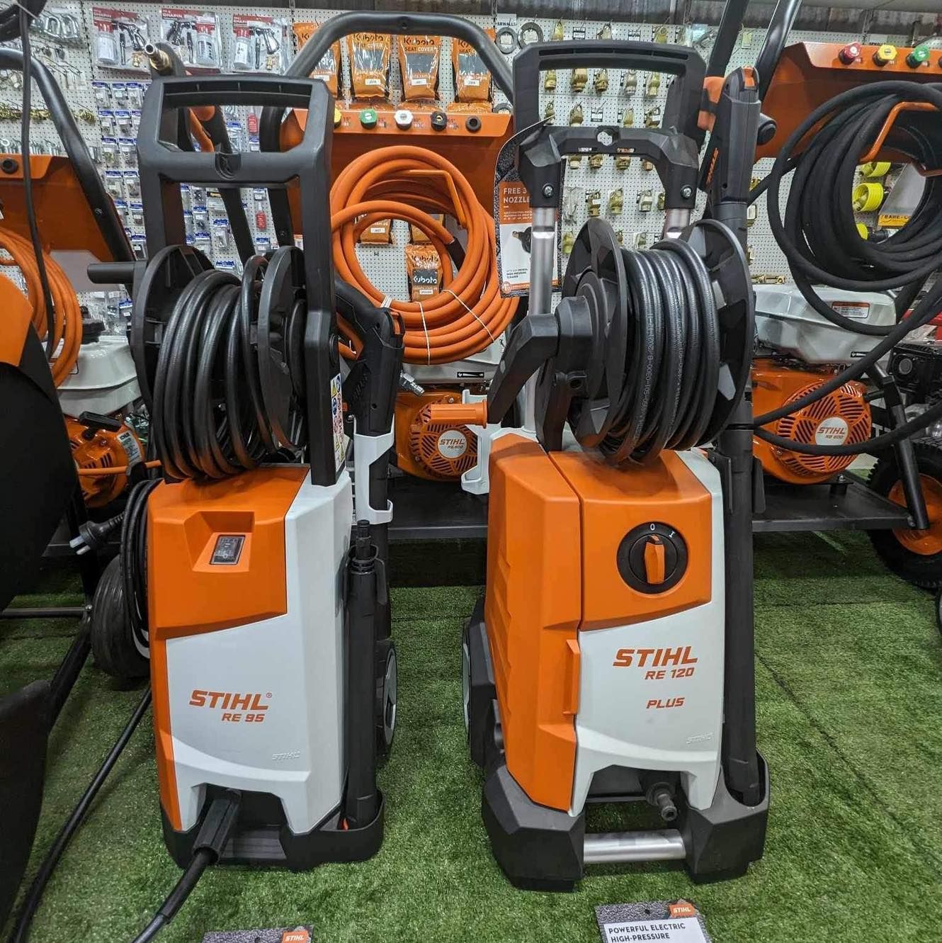 Two Stihl Pressure Washers, Orange and White, Displayed With Coiled Hoses on a Store Rack — Casali's in Mareeba, QLD