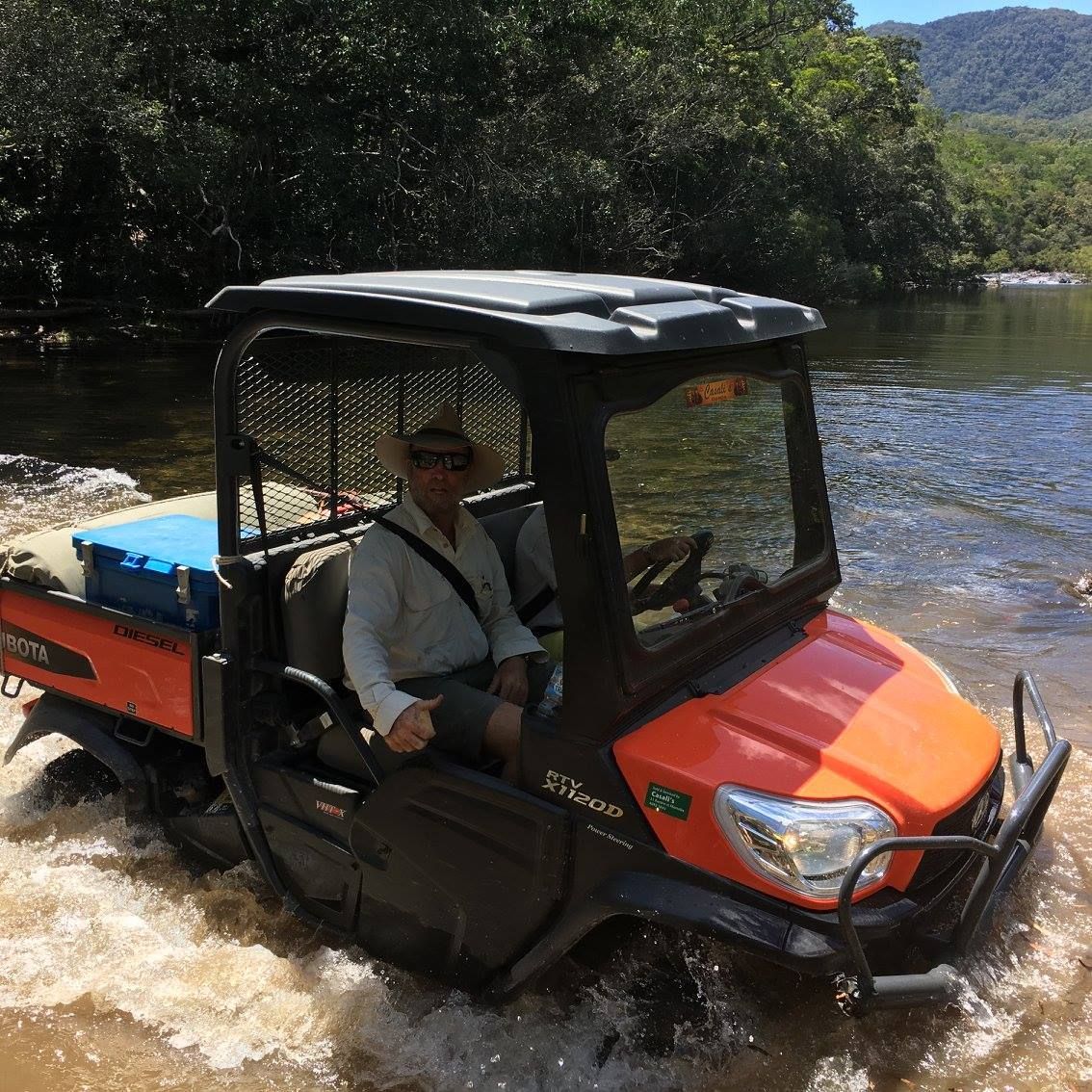 Orange Utility Vehicle Driving Through Shallow River Water in a Wooded Area — Casali's in Mareeba, QLD