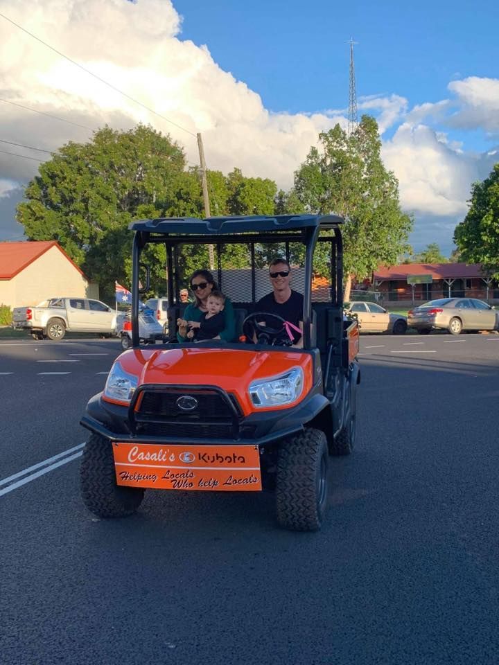 Two People Riding in an Orange Off-road Utility Cart on a Street Under a Blue Sky — Casali's in Mareeba, QLD