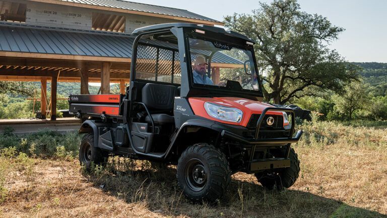 Red UTV parked on dry grass beside a house with a tiled roof, under trees in a sunny rural setting. — Casali's in Mareeba, QLD