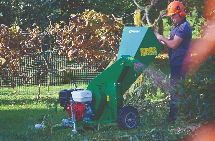 Person Using an Orange Wood Chipper in a Leafy Yard, Feeding Branches Into the Machine — Casali's in Mareeba, QLD