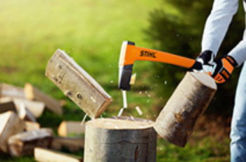 Person Splitting a Log With an Orange Axe Beside a Stack of Firewood Outdoors — Casali's in Mareeba, QLD