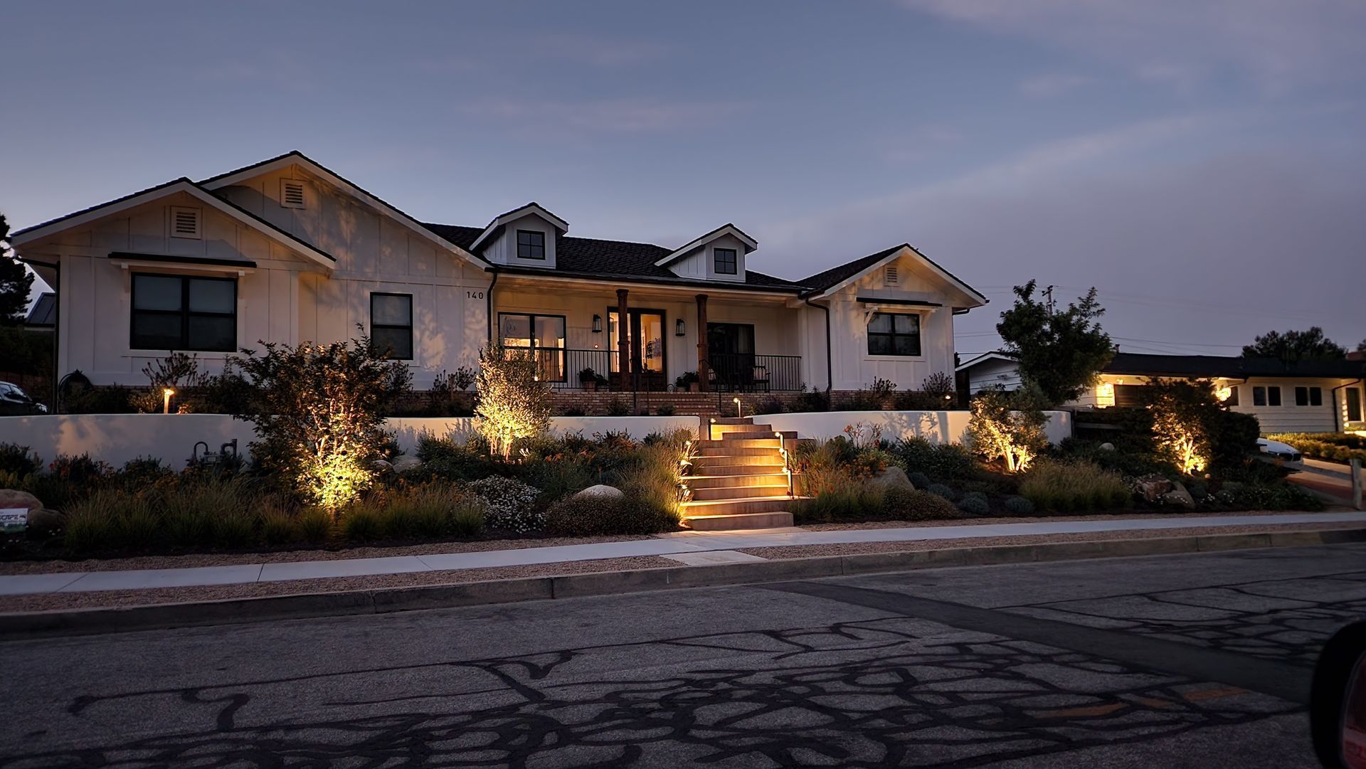 Large suburban house at dusk with warm exterior lights and a lit front walkway