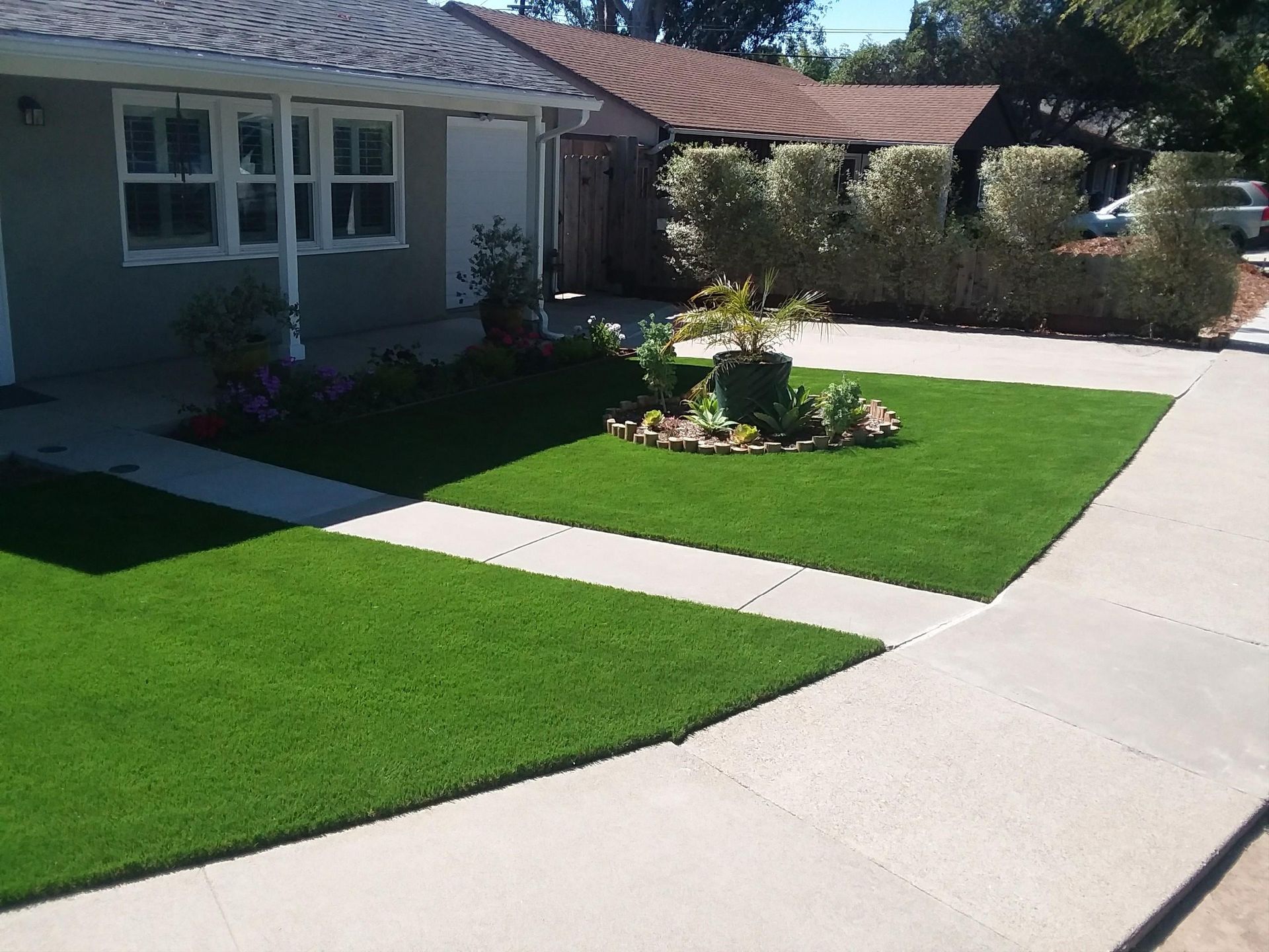 Suburban front yard with green lawn, flower bed, and a curved driveway beside a house.