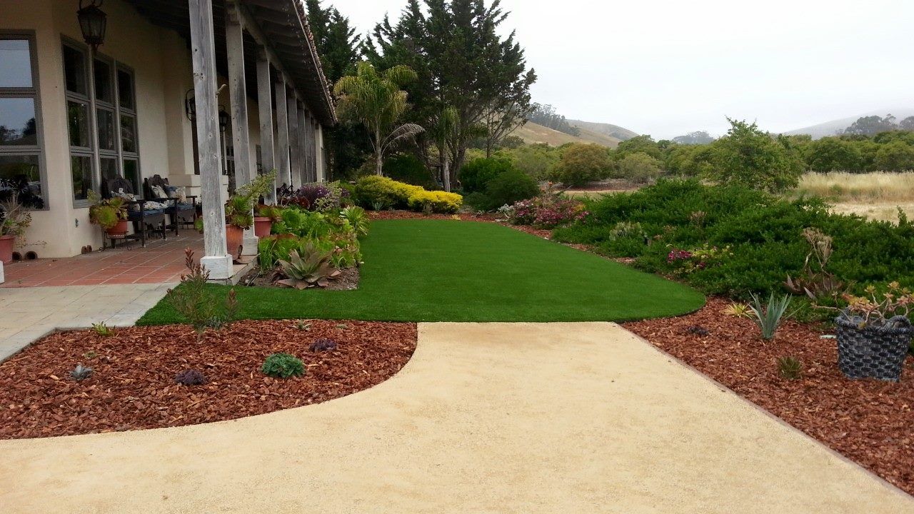 Landscaped garden path with green lawn, flower beds, and a house porch on the left