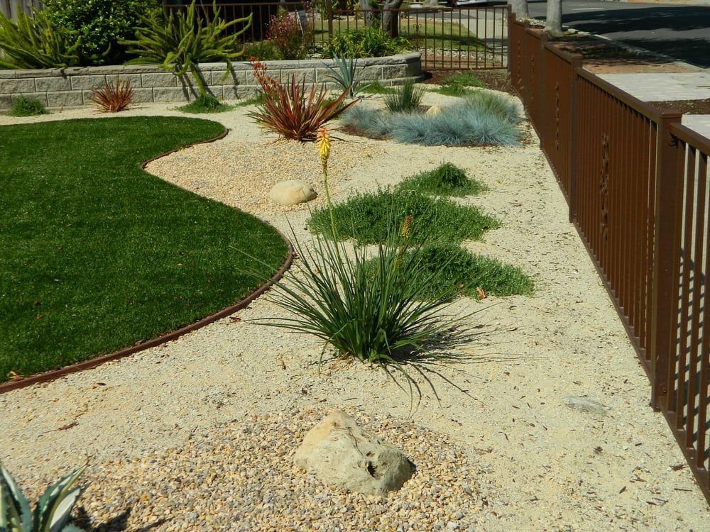 Landscaped yard with white gravel, green grass, and decorative plants beside a wooden fence