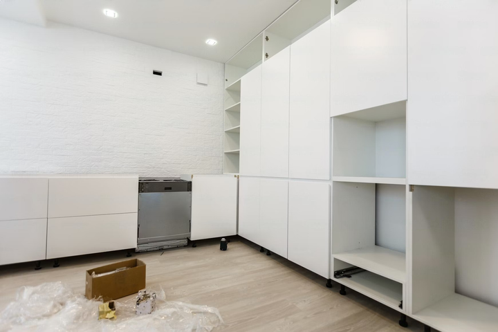 Bright white kitchen under renovation with built-in cabinets, boxes, and tools on the floor.