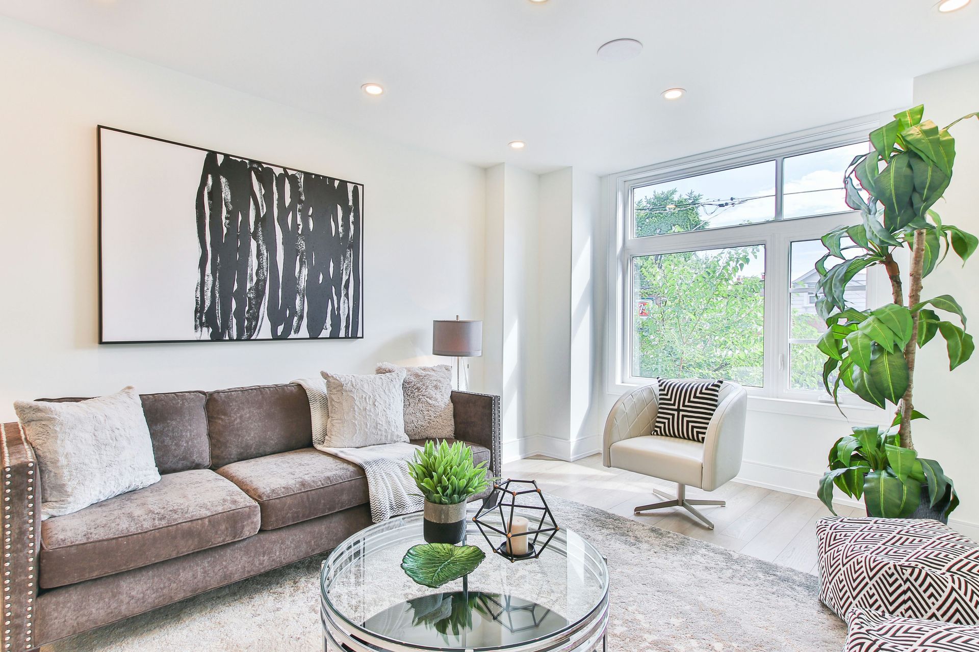 Bright modern living room with gray sofa, abstract wall art, large window, and potted plant.