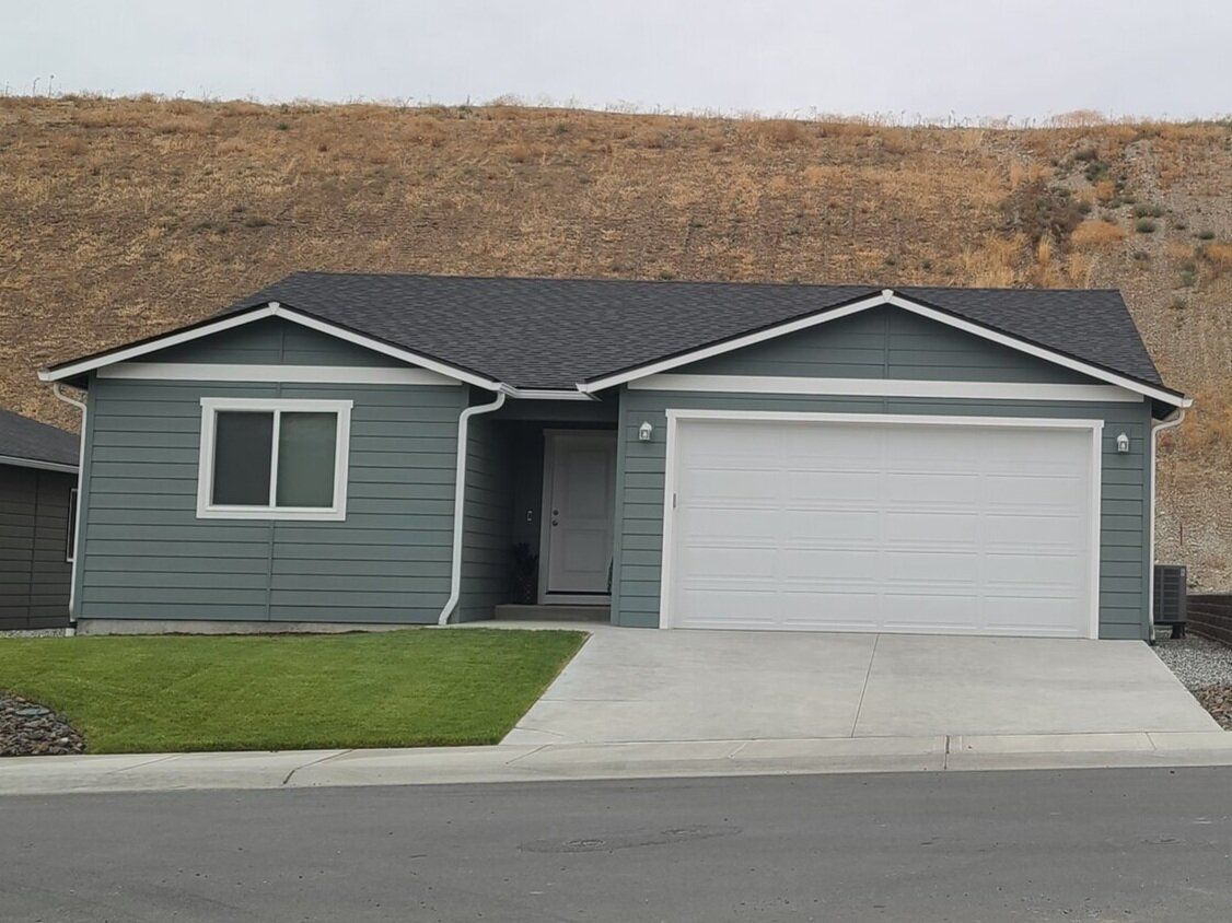 A small house with a garage and a hill in the background.