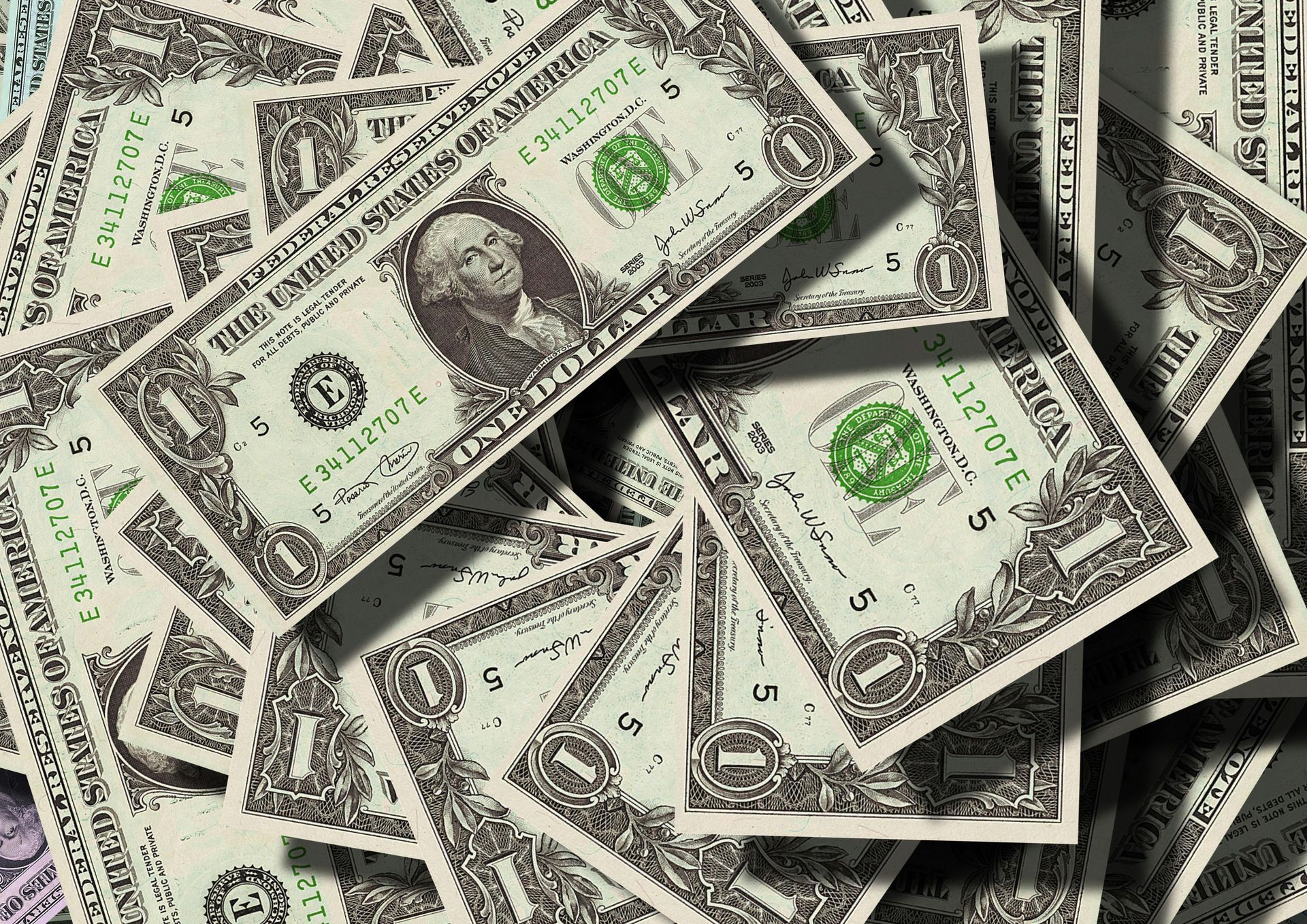 Pile of United States one-dollar bills, green and white, scattered.
