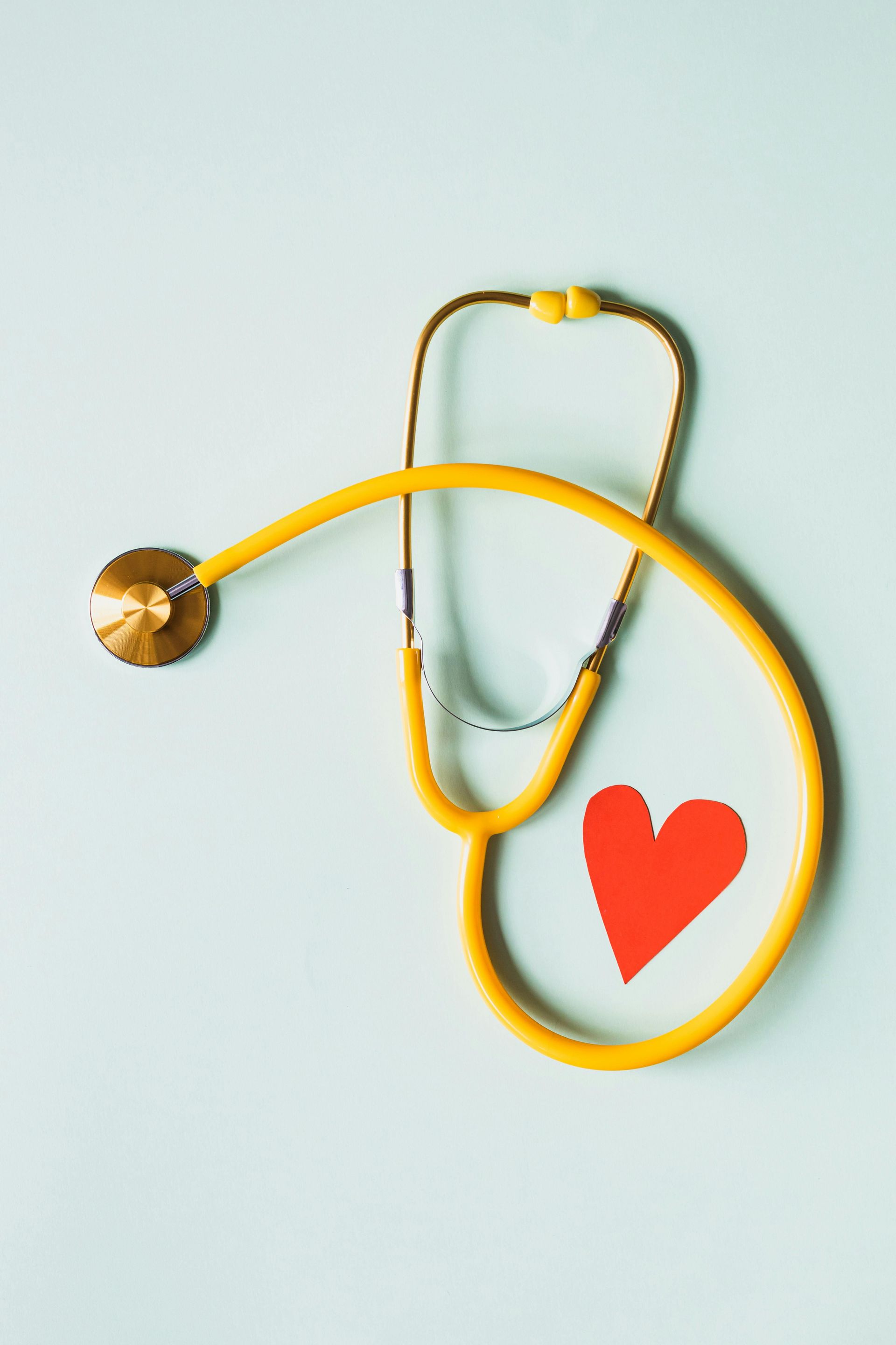 Yellow stethoscope and red heart on a light blue background, symbolizing healthcare.