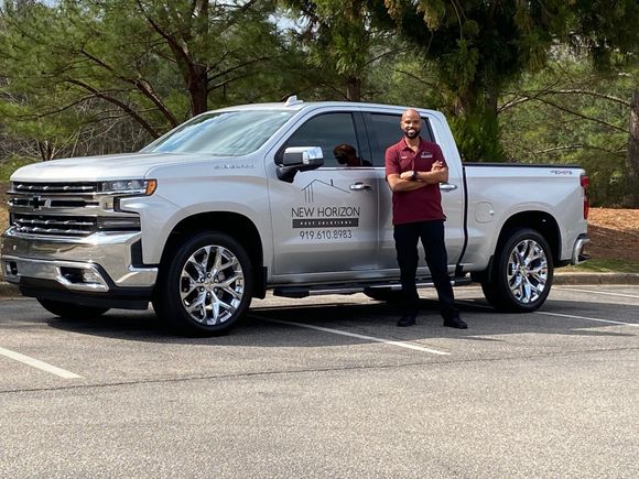 A man is standing next to a silver truck in a parking lot.