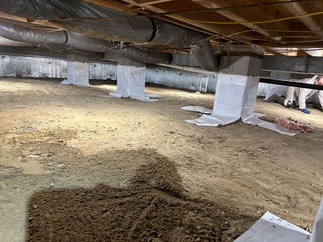 A man is working underneath a house with a lot of pipes.