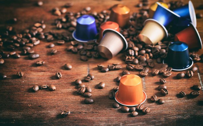 Capsule di caffè colorate sparse tra chicchi di caffè su una superficie di legno