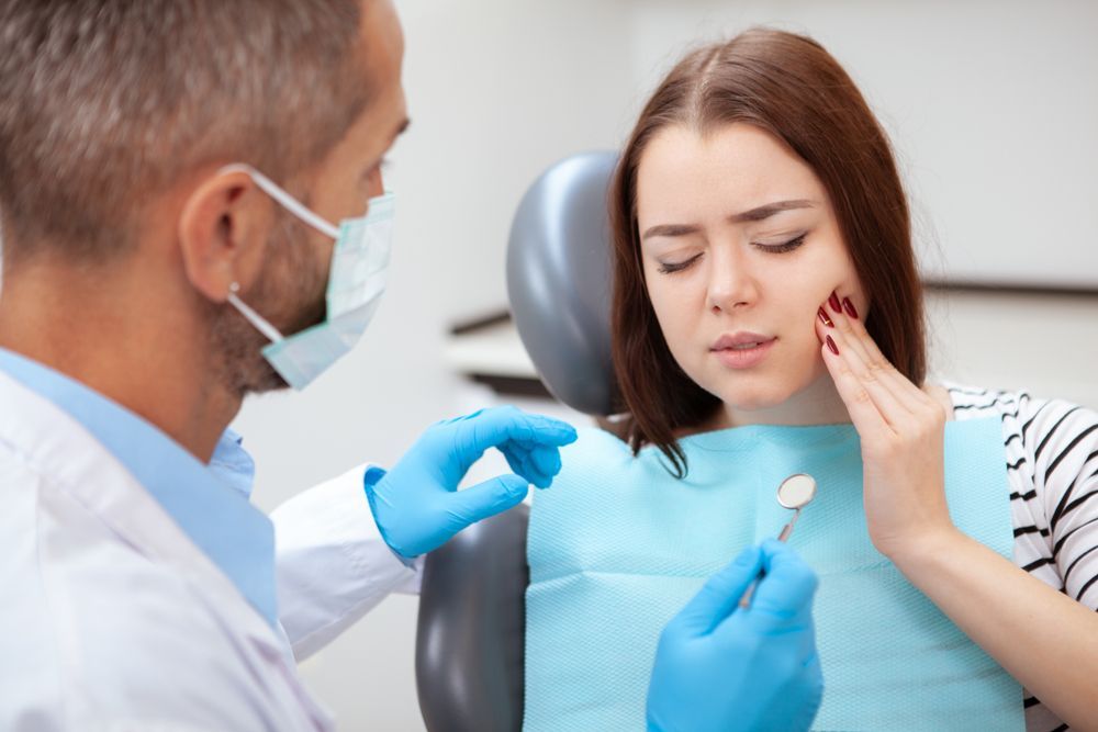 Dentist Examining a Patient With a Hand on Her Cheek, Expressing Pain in a Dental Office
