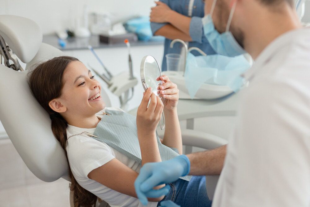 A Little Girl Is Sitting In A Dental Chair Looking At Her Teeth In A Mirror — St Ives Dental Boutique In Saint Ives, NSW
