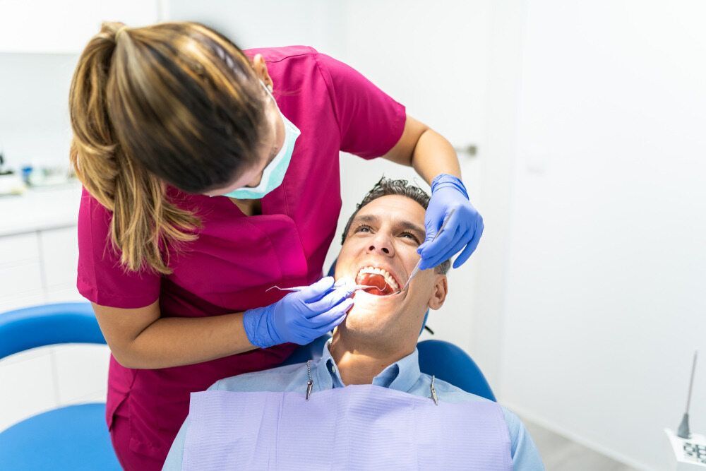 A Man Is Sitting In A Dental Chair While A Female Dentist Examines His Teeth — St Ives Dental Boutique In Saint Ives, NSW