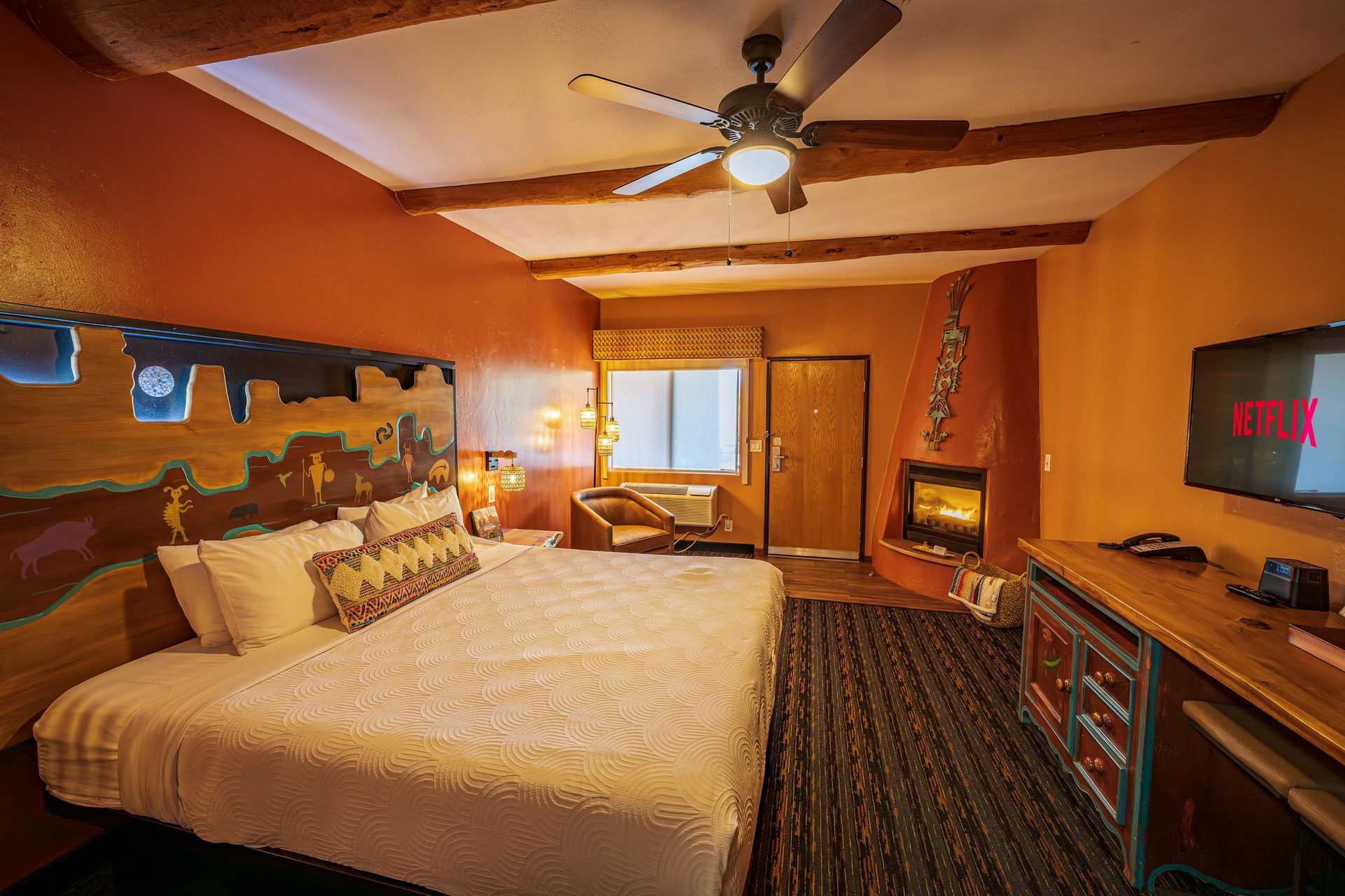 Warm bedroom with orange walls, large bed, ceiling fan, window, and TV stand.