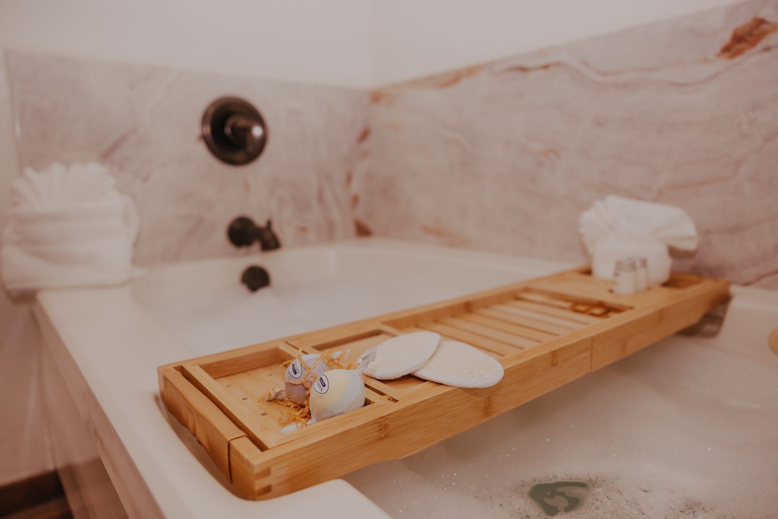 Bubble bath with a wooden tray holding a candle, cup, and towel in a marble tub