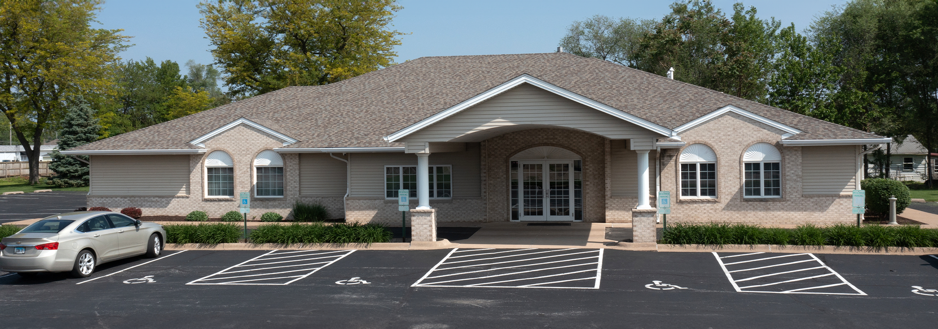 Exterior view of a one-story brick building with a car parked in front of it and a handicapped parking spot.