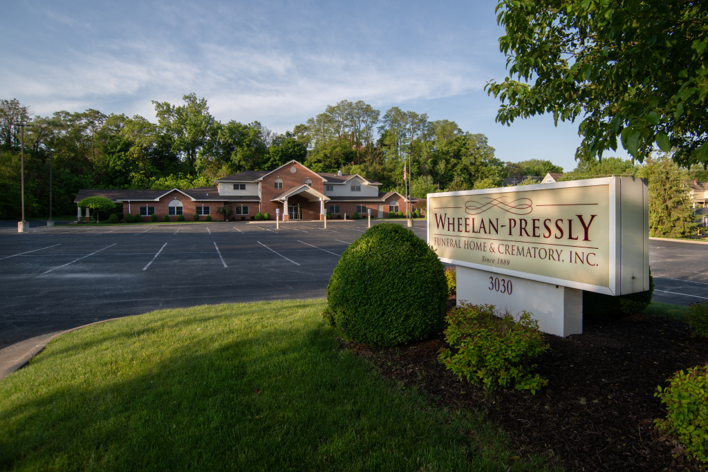 William Pressly Funeral Home sign and brick building. Empty parking lot and green grass with trees.