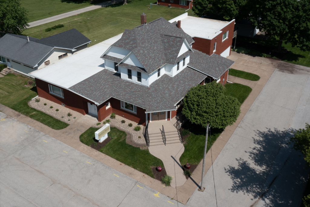 Aerial view of a white and red brick building with a gray roof, in a residential area.