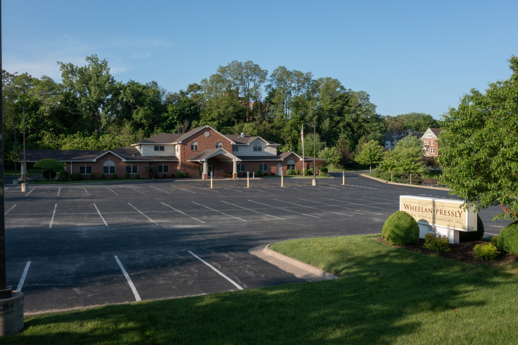 Empty parking lot in front of a brick building with trees in the background under a blue sky.