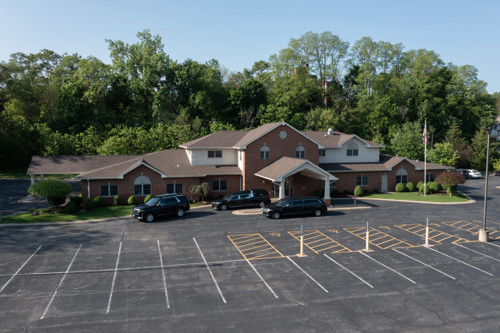 Exterior view of a brick building with several dark vehicles parked in front, and a large empty parking lot.
