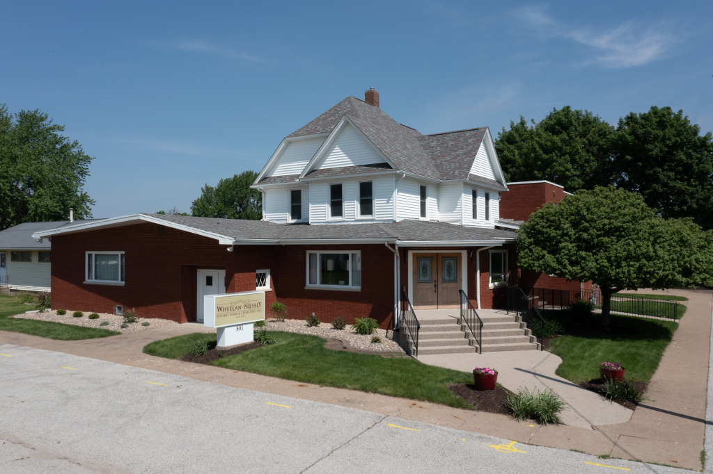Two-story white house with a brick addition, on a sunny day. Steps lead to a double-door entrance.