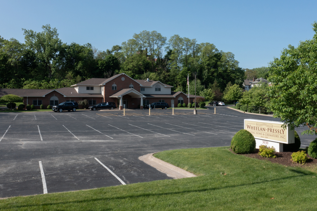 Building with large parking lot, trees in the background, and sign.