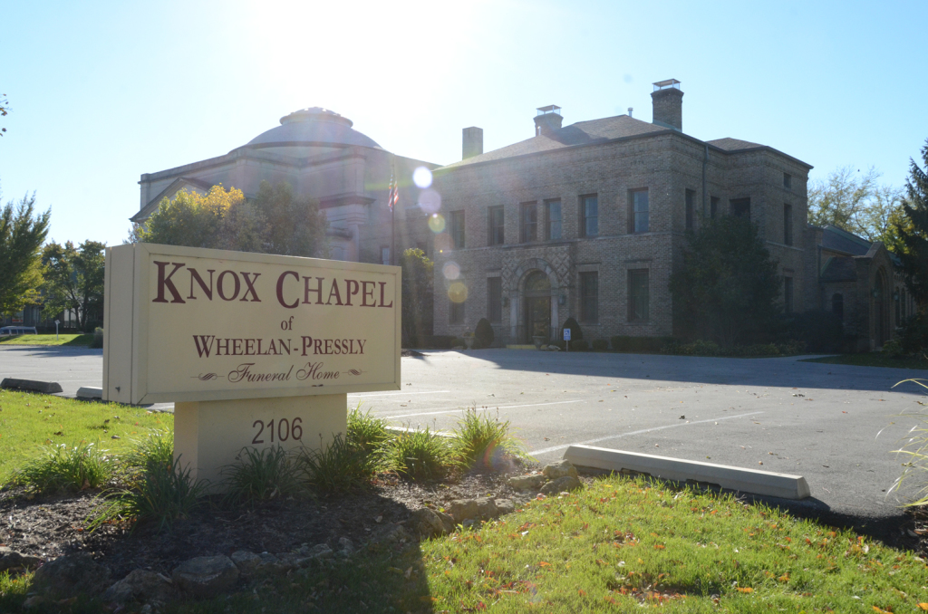 Sign for Knox Chapel at Whelan Park, 2106, with two stone buildings and sun glare.