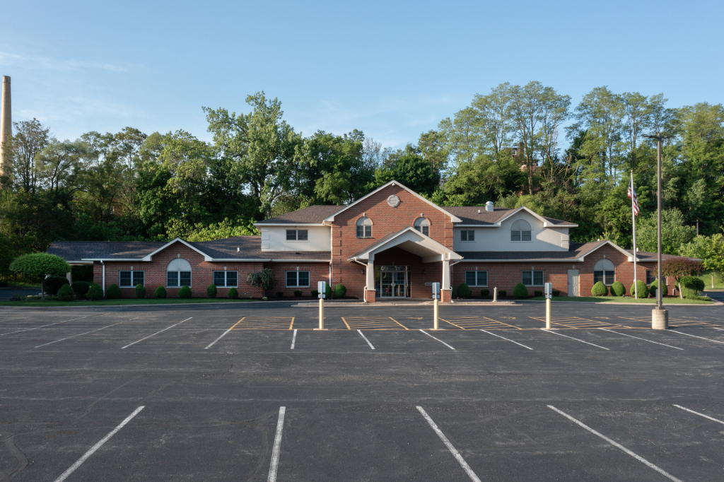 Brick building with large parking lot, trees in background, blue sky.