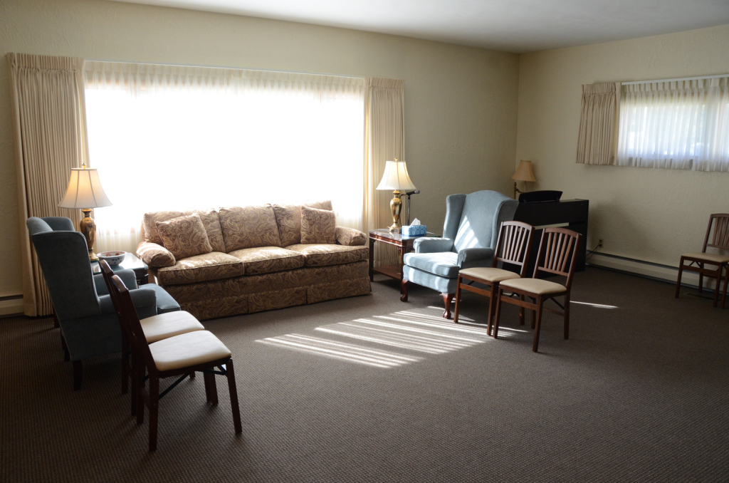 A waiting room with chairs, sofas, lamps, and a large window with sunlight.