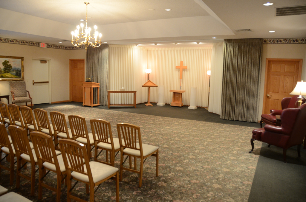 Funeral home interior with chairs facing an altar area; gold tones, neutral carpet.