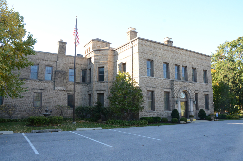 Brick building with an American flag, trees, and a parking lot.