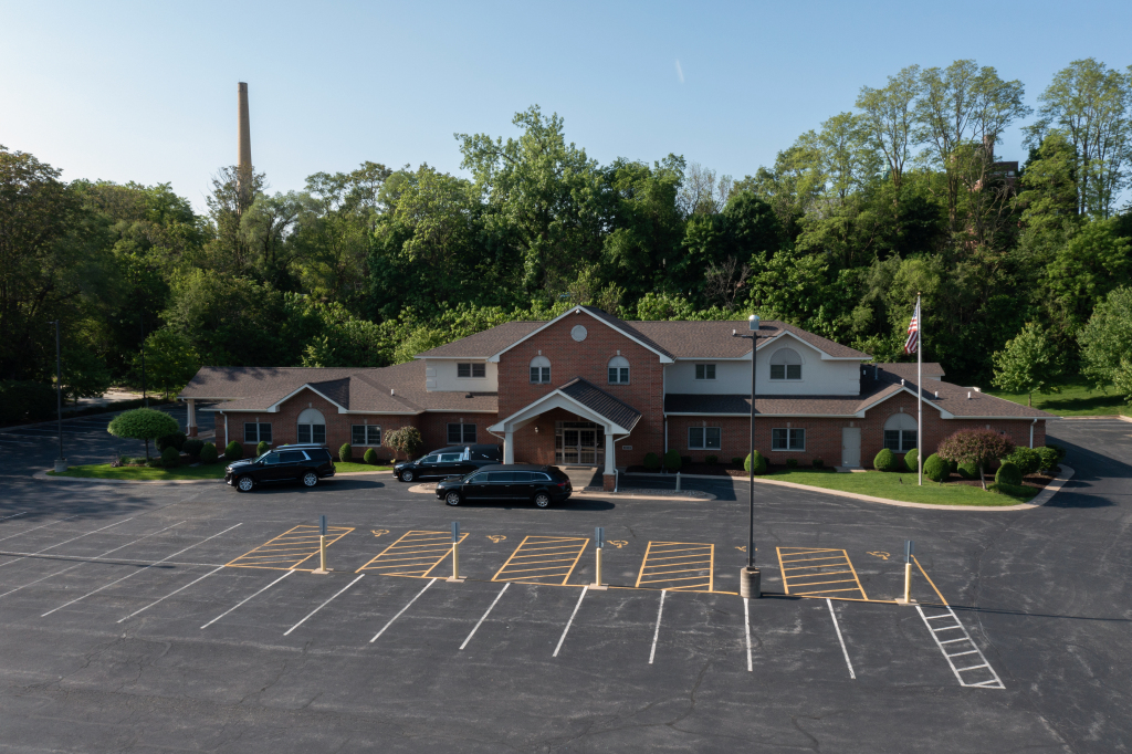 Brick building with parking lot. Cars parked in front. Trees in the background.