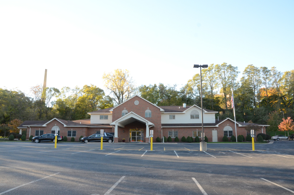 Building with brick facade, large parking lot. Entrance canopy. Trees in background.