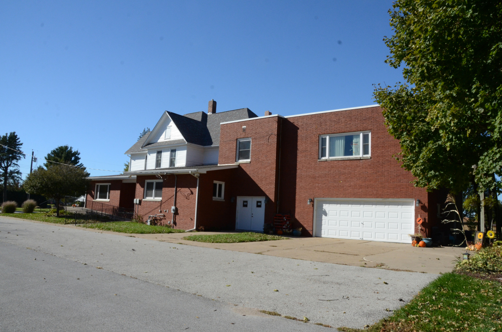 Two-story brick building with white garage door and adjacent white house, under clear blue sky.