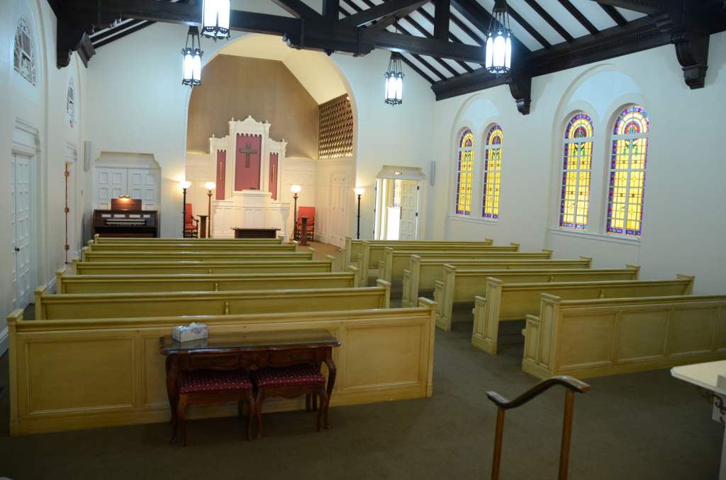 Interior of a church with wooden pews, stained glass windows, and a raised altar area.
