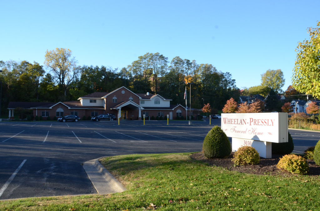 Red & Freshia Funeral Home, exterior view. Building with red brick, parking lot, and sign.