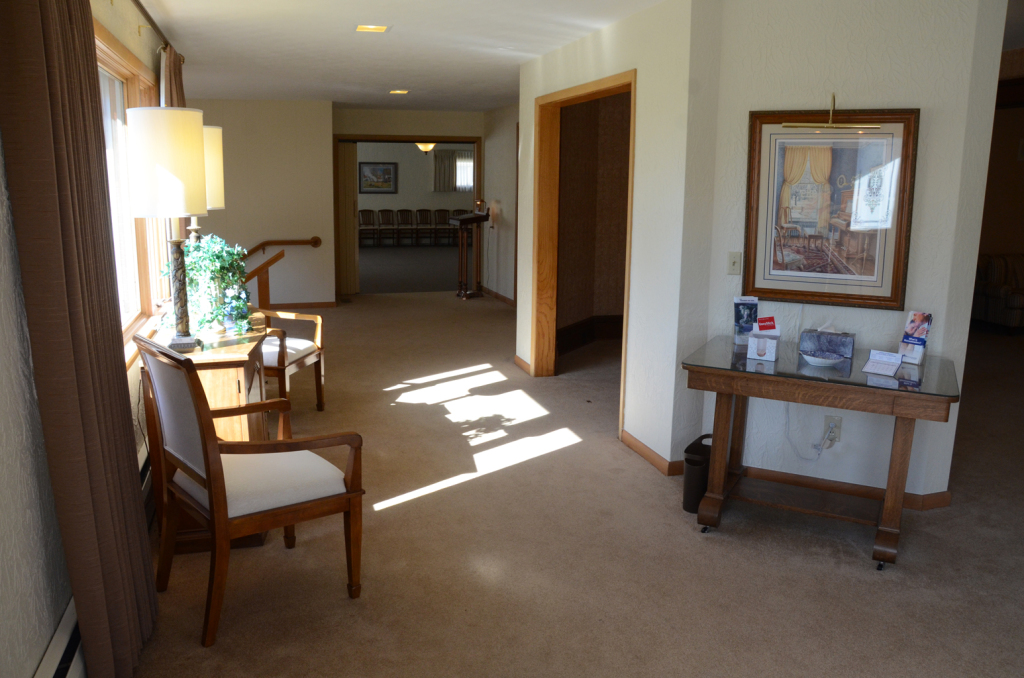 Hallway with chairs, table, and artwork. Natural light streams in.
