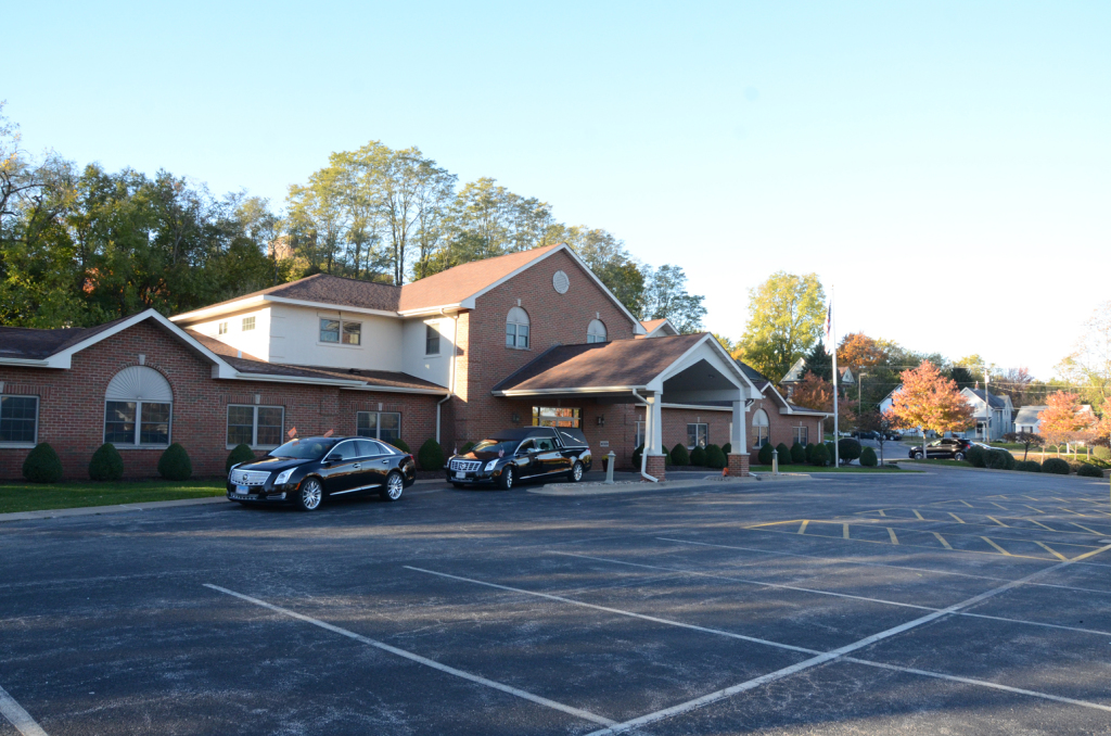 Brick building with a covered entrance, several black cars parked outside, and a large parking lot.