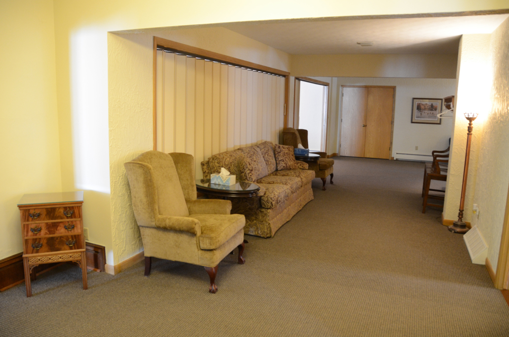 Interior of a room with a sofa, chair, window, and a small wooden cabinet.