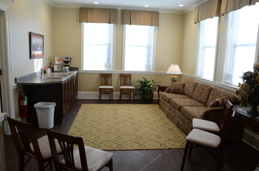 Waiting room with sofa, chairs, rug, windows, and coffee station.